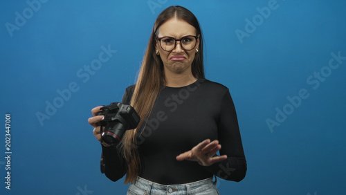 Bild auf Leinwand Woman holding dslr camera with raised hand and grimacing face showing disgust while checking lens in studio; disgust rejection
