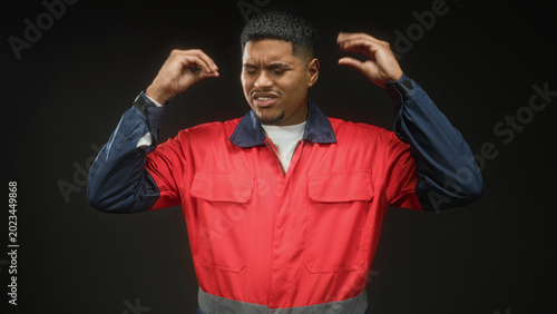 Schilderij op canvas Man in red uniform grips his head with both hands, grimacing in studio; frustration strain fatigue work