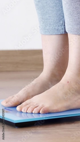 Close-up of a young woman weighing herself on a scale at home and throwing measuring tape on the blue scale.
