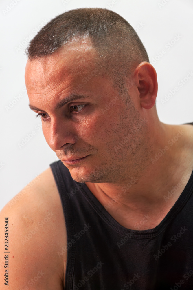 Naklejka premium Man with Short Buzz Cut Hair Looking Down Against Plain Background neutral grey studio wall.