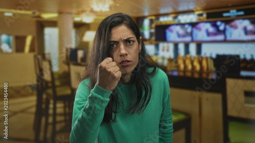 Cuadro en lienzo Woman clenches fist and glares in a restaurant building with raised hand near face and furrowed brow, leaning forward in an aggressive stance; anger confrontation