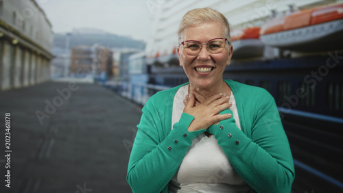 Tableau sur toile Woman middle aged smiling with hands on chest on cruise ship near terminal building outdoors; gratitude warmth