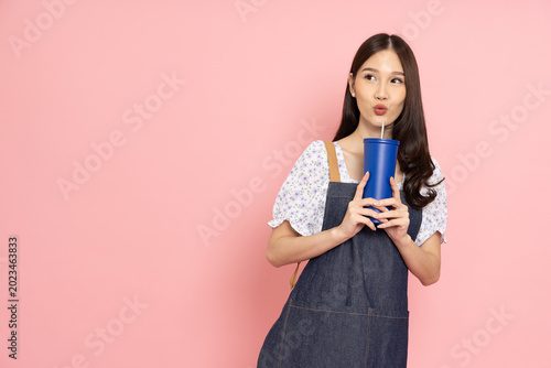 Schilderij op canvas Cute Asian woman wearing a denim apron holds a blue reusable tumbler, looking as