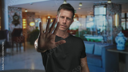 Bild auf Leinwand Man in black t shirt with hand palm forward to camera stop in hotel building lobby; defiance boundary privacy