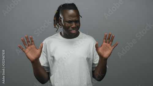 Принти на полотні Young african american man in white t shirt with palms up and hands raised in a gray studio; disgust avoidance hesitation