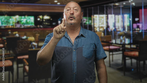 Tableau sur toile Man points finger at camera in a restaurant building, raising index finger in a clear pointing gesture; assertive warning