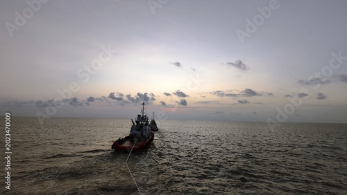 Foto A rear view of a tugboat in the middle of the ocean during twilight, showing the towing line submerged in the water under a soft evening sky