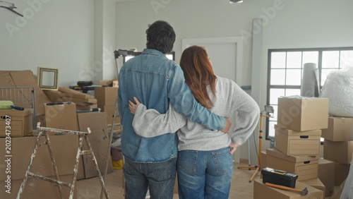 Tableau sur toile Man embraces woman with arm around waist among stacked moving boxes in a building; hopeful new start