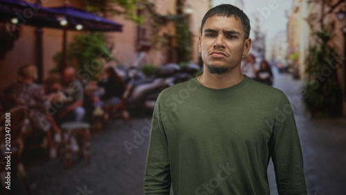 Canvastavla Man with frowning face standing in street cafe, arms at sides, looking at camera; subtle discontent