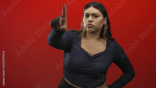 Vászonkép Woman points finger with outstretched hand and visible finger gesture in studio, stern expression; disapproval boundary setting