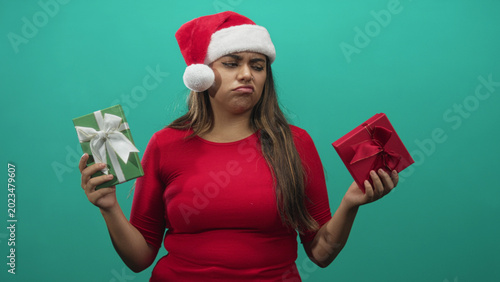 Canvas Print Woman holding two wrapped gifts with pouting face wearing santa hat in studio; disappointment indecision