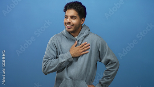 Konstfotografi Man with hand on chest in blue studio backdrop wearing hoodie in a pledge gesture; sincerity reflection focus
