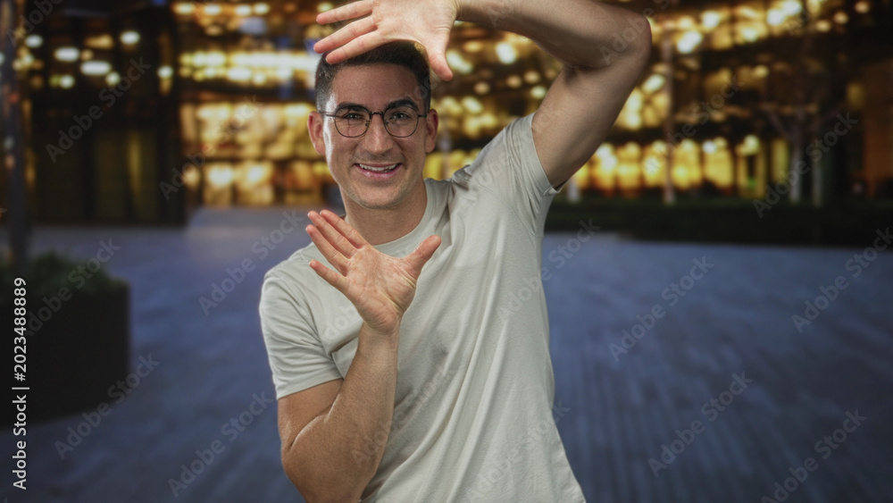 Fototapeta premium Man framing with hands and smiling in front of illuminated building at night; playful creativity inspiration.
