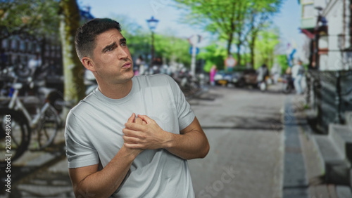 Man clutching chest with heartattack on crowded city street near parked bicycles and lampposts; panic urgent medical help.