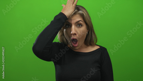 Foto Woman opens mouth and places palm to forehead with widened eyes against green studio backdrop; surprise