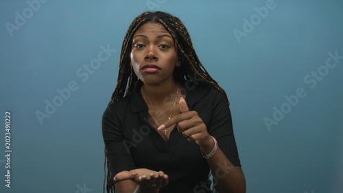 Cuadro en lienzo Woman with braided hair wearing a cross necklace showing open hands and palms up gesture in a studio against a blue wall; pleading apology