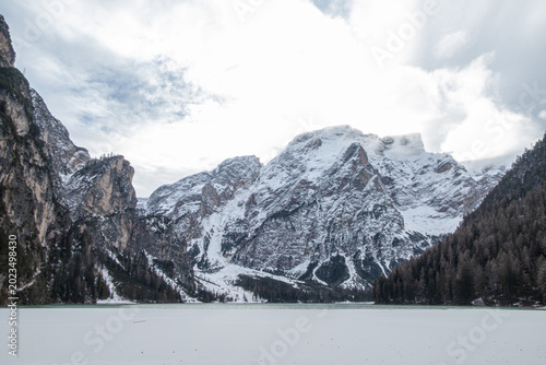 Obraz na plátně A wide winter landscape of the frozen surface of Lake Braies (Prags) in the Dolomites, showcasing the massive snow-covered peak of Seekofel under a bright cloudy sky