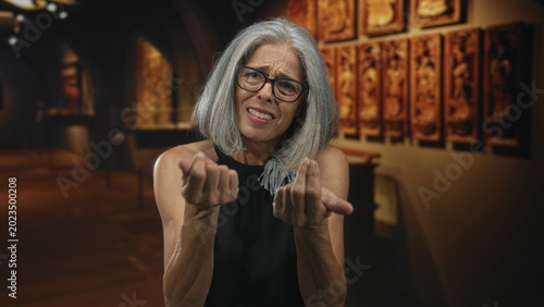 Foto Woman displaying palms up pleading gesture in gallery building beside framed artwork and dim arches; uncertainty plea confusion