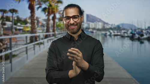 Valokuva Man clapping hands on a street pier at a marina, wearing glasses and beard and smiling into camera; celebration joy