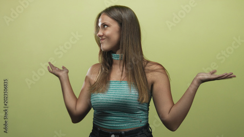 Canvas Print Woman shrugging palms up with a coy smirk, turquoise strapless top and choker visible in a midshot against a green studio wall, hands raised in a questioning gesture; uncertainty