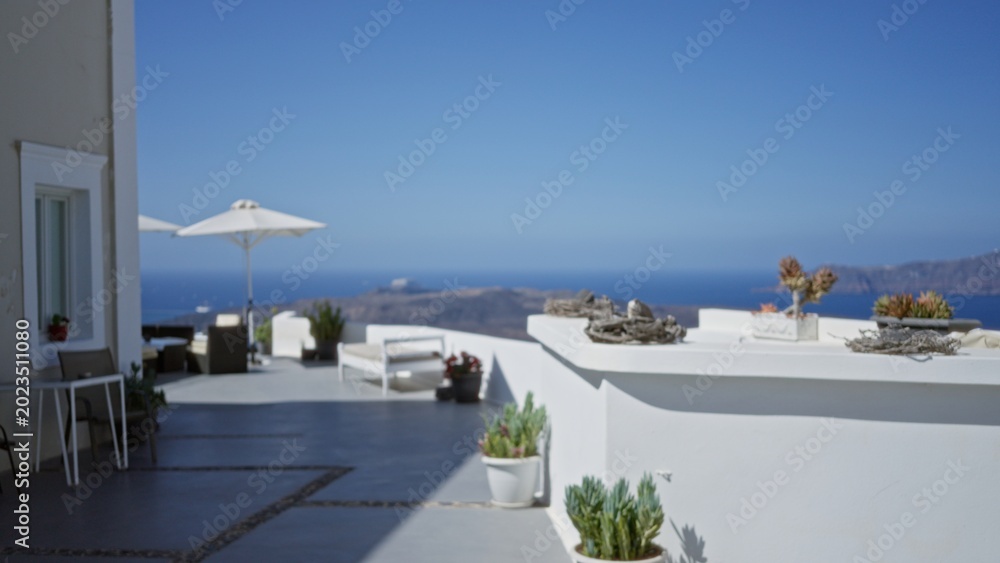 Fototapeta premium Sunlit seaside terrace with defocused foreground, soft bokeh sea and white architecture, outdoor; background backdrop copyspace calm.