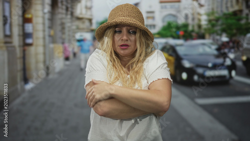 Foto Woman with hands covering mouth on a street wearing straw hat and white dress, arms drawn to chest; surprise vulnerability