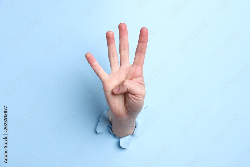 Naklejka premium Woman showing number four with fingers through hole in light blue paper, closeup