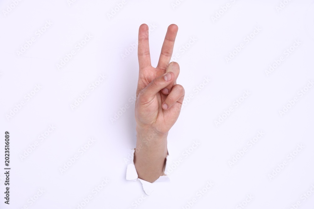 Naklejka premium Man showing number two with fingers through hole in white paper, closeup