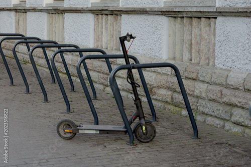 Electric kick scooter parked and locked near bicycle rack on city street against stone building wall in urban environment. Modern eco friendly transportation and micromobility concept in Europe.