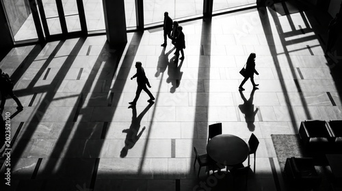 A group of people silhouetted as they walk across a spacious, modern lobby, casting long shadows from the light filtering through large windows
