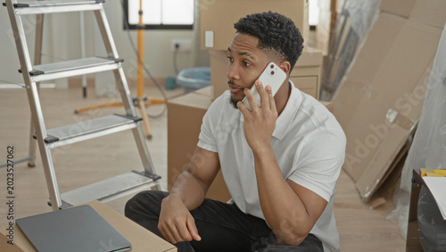 Bild auf Leinwand Man holds smartphone to ear while sitting among moving boxes and ladder in a building; focused planning