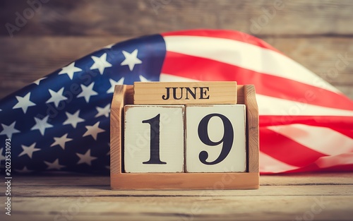 June 19th date on wooden calendar blocks with american flag background on weathered wood table