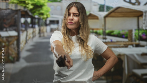 Bild auf Leinwand Middle aged woman pointing finger forward with hand on hip in street market aisle; disapproval confrontation