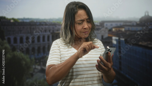 Foto Woman tapping smartphone screen on building balcony, holding phone with both hands and frowning slightly; concentration problem solving