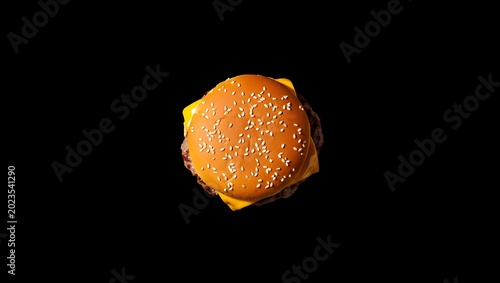 Top view of a fresh cheeseburger with sesame seed bun and melted cheese on a dark background