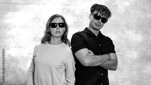 Foto Young man and woman in sunglasses standing back to back, depicting cool fashion