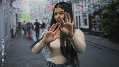 Cuadro en lienzo Latin woman pinches nose on bustling city street in front of storefronts to block foul odor; disgust