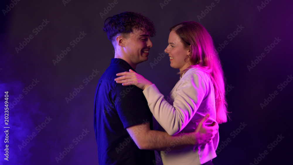 Obraz premium Couple dancing and embracing, happy and romantic, against a background of purple and pink neon light