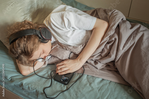 Photos Teen Falling Asleep with Headphones and Smartphone in Bed, for Digital Detox Top