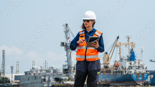 Professional woman in safety uniform monitoring global trade and shipping cargo operations.