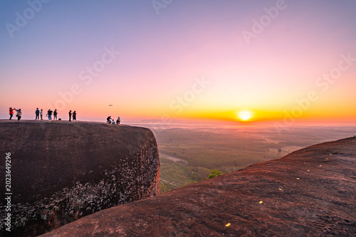 Foto Morning light bathes the sandstone ridge in gold as visitors admire the horizon, their dark silhouettes contrasting beautifully with the expansive natural scenery