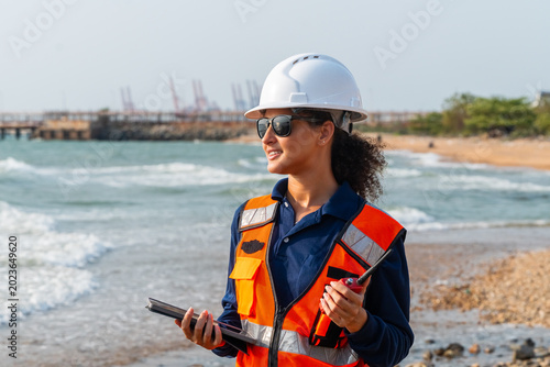 Canvastavla Corporate ESG and CSR industrial compliance: Confident female marine ecologist using tablet and walkie-talkie for offshore terminal logistics and coastal environmental sustainability