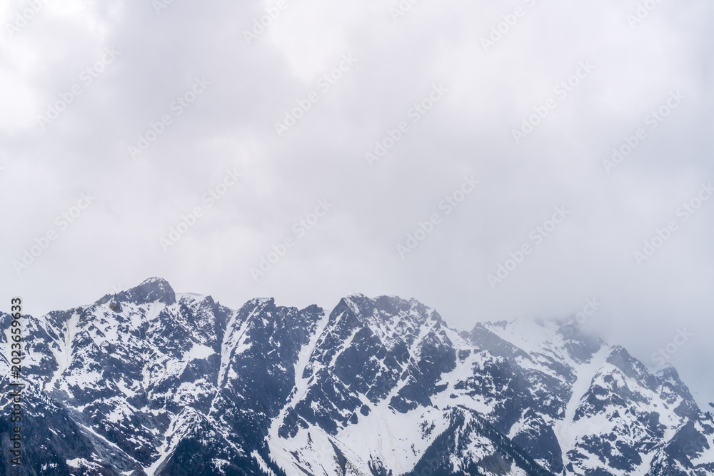Obraz premium Jagged snow covered mountain peaks beneath storm clouds in British Columbia