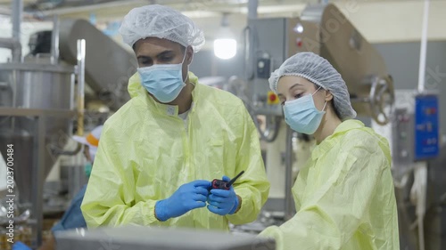 Food factory automated production line, Sterile factory worker inspection production line cleanroom with protective suit and face mask, industrial safety uniform and blue glove quality control