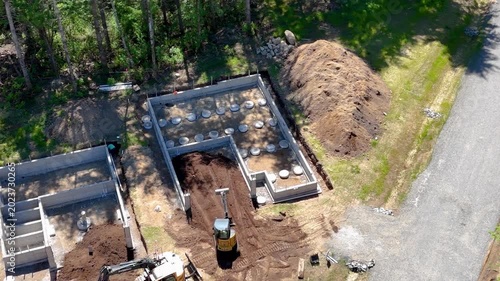 Aerial circling view of a mini excavator grading soil within a residential concrete foundation
