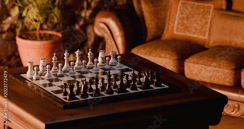 Fotografie Wooden chessboard on coffee table, cozy living room with leather armchair, 3D re