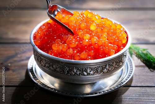Red, granular caviar, a tasty, valuable product in a spoon and silverware on a black background. Close-up.