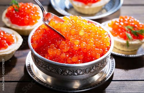 Red, granular caviar, a tasty, valuable product in a spoon and silverware on a black background. Close-up.