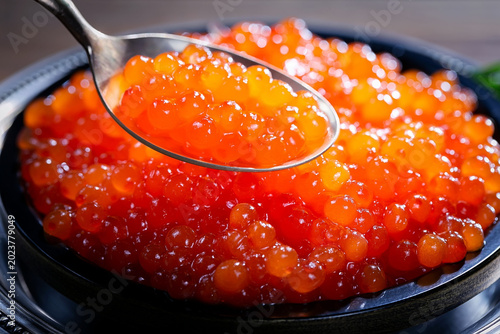 Red, granular caviar, a tasty, valuable product in a spoon and silverware on a black background. Close-up.