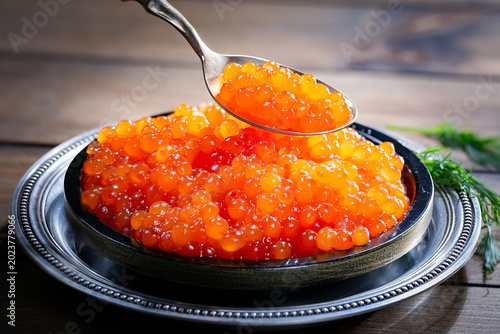 Red, granular caviar, a tasty, valuable product in a spoon and silverware on a black background. Close-up.